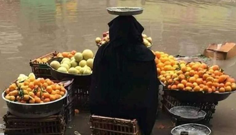 مسنة تبيع الفاكهة وسط هطول الأمطار بمصر