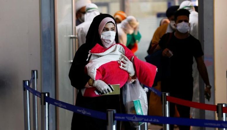 امرأة ترتدي قناعا واقيا وهي تحمل طفلها في إيران