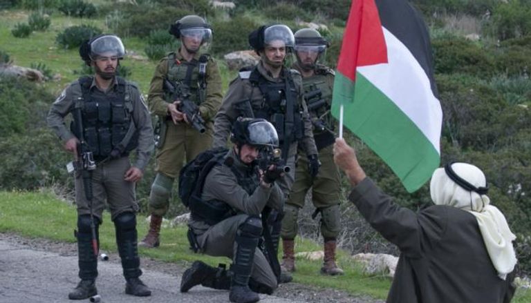 جندي إسرائيلي يصوب سلاحه نحو مسن فلسطيني