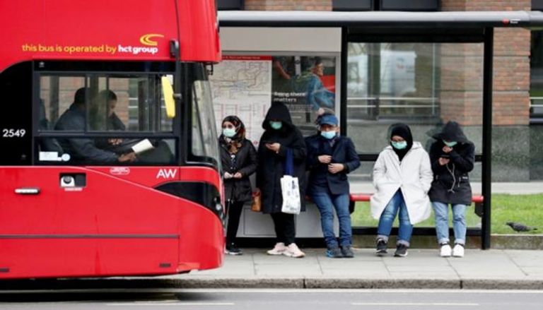 أشخاص يرتدون كمامات وينتظرون حافلة في لندن