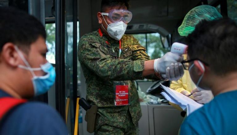 جندي يفحص درجة حرارة الجسم لعاملين صحيين في مترو مانيلا بالفلبين