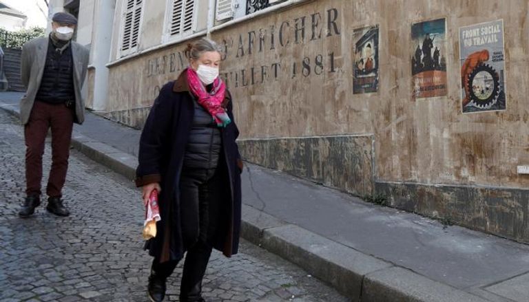 فرنسيان يرتديان الكمامة في أحد شوارع باريس