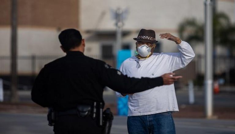 شرطي أمريكي يتحدث إلى رجل يرتدي قناعا للوجه كإجراء وقائي ضد كورونا 