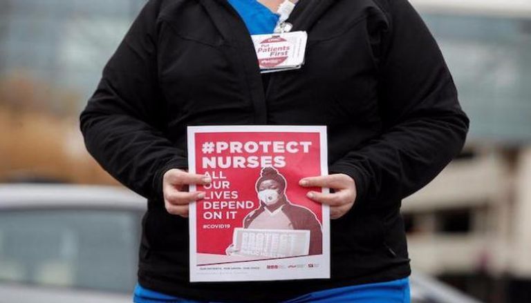 ممرضة تحمل ملصقا يدعو لحماية العاملين بالتمريض