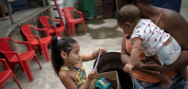 فتاة صغيرة تحمل علبة مليئة بالمواد الغذائية ومواد التنظيف