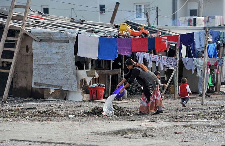 سيدة من غجر الروما أمام سلة مهملات تتكدس فيها القناني البلاستيكية