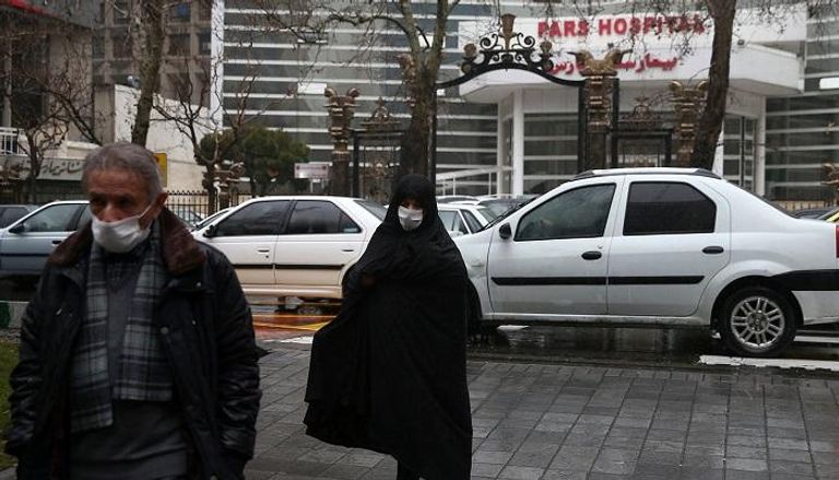 شخصان يرتديان الكمامات أمام أحد مستشفيات طهران