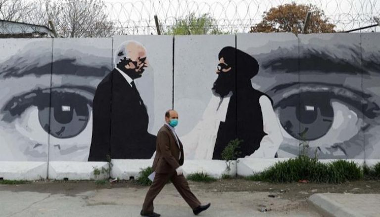 أفغاني يرتدي قناعا أمام صورة لخليل زاد والملا عبدالغني بارادار