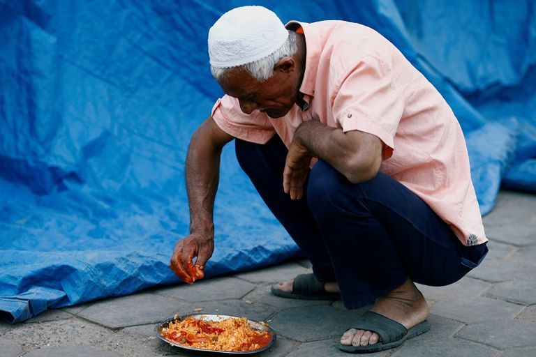 مسلم يتناول طعام فطوره بجوار مسجد مع حلول أذان المغرب
