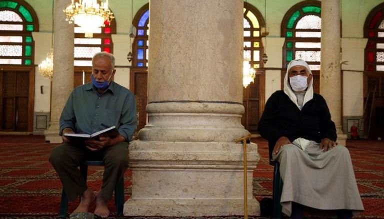 رجلان يرتديان كمامات للوقاية من كورونا بأحد مساجد دمشق