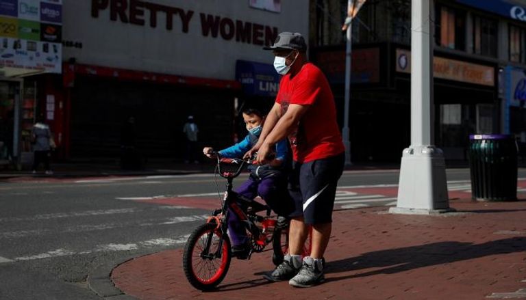 رجل يساعد طفلا على ركوب دراجة وهو يرتدي كمامة في نيويورك