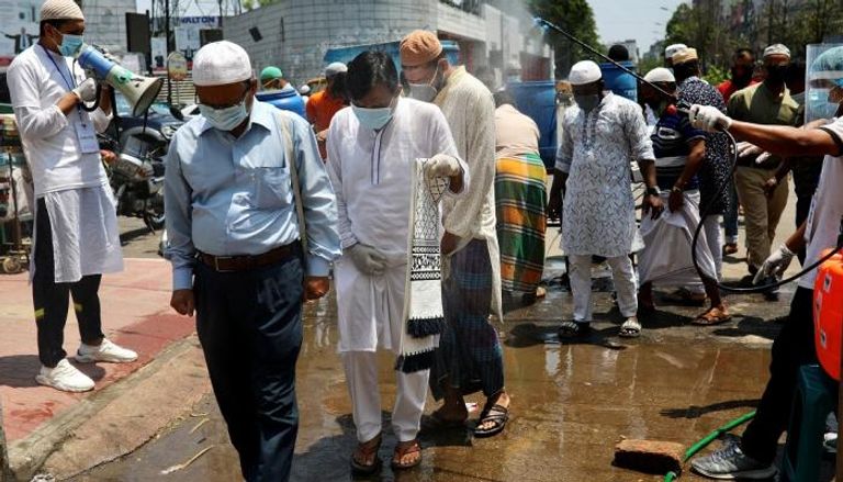 رجال يرشون مصلين بالمطهرات قبل دخول مسجد في دكا