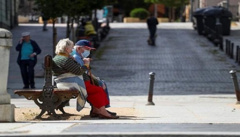 عجوزان يجلسان مرتديان الكمامة خشية كورونا- أرشيفية