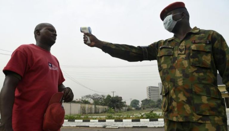 جندي يفحص درجة حرارة مواطن في نيجيريا  