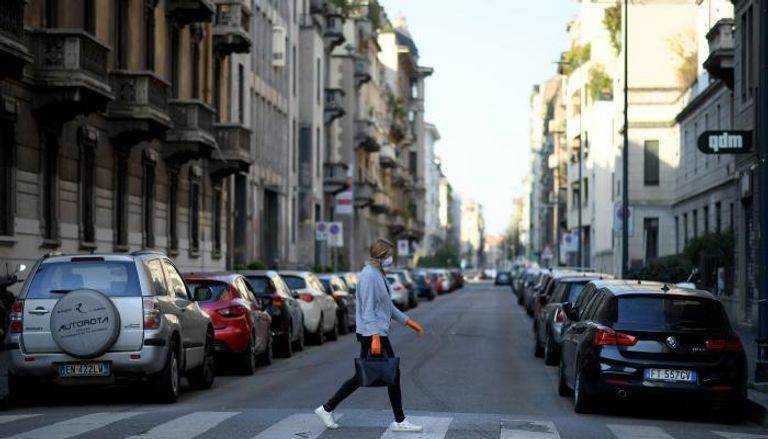 امرأة ترتدي قناع وجه واقٍ تعبر أحد الشوارع في ميلانو