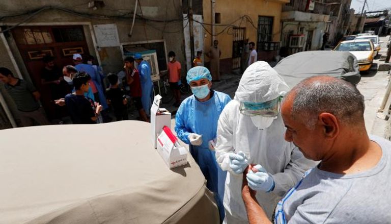عاملون صحيون يأخذون عينة دم من مواطن عراقي