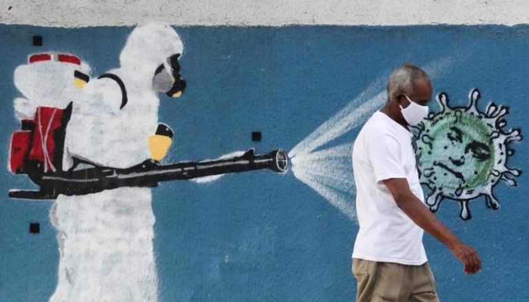 برازيلي يرتدي الكمامة ويسير بجوار حائط عليه جرافيتي عن مكافحة الفيروس