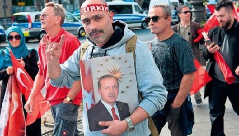 تركي بألمانيا يحمل صورة أردوغان ويشير بشعار الذئاب الرمادية