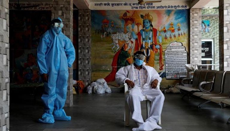 رجل دين في الهند يرتدي كمامة وإلى جواره حارسه الشخصي