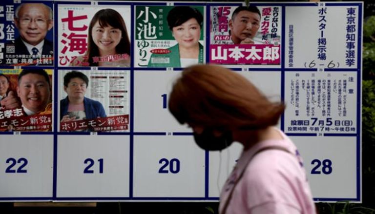 يابانية تمر بجوار لافتة تحمل صور المرشحين 