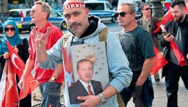 تركي يحمل صورة أردوغان ويشير بشعار الذئاب الرمادية
