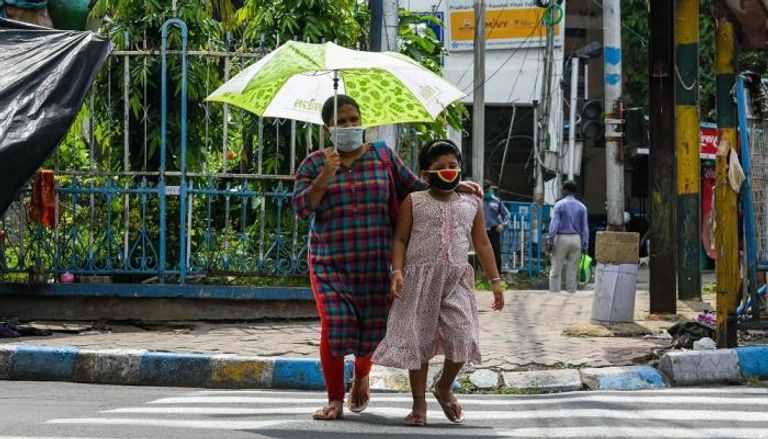 أم وابنتها ترتديان قناعا بينما تعبران طريقا في مدينة كلكتا الهندية