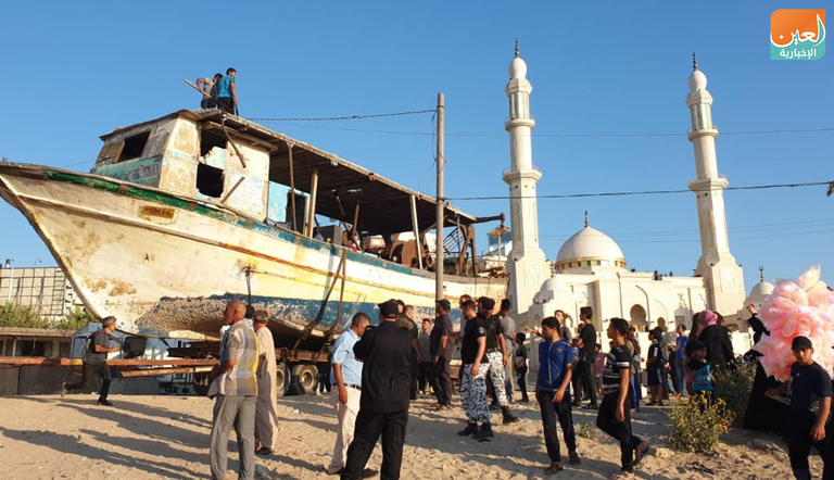 صيادون ينظرون لقارب متهالك قوارب صيد على شاطئ غزة