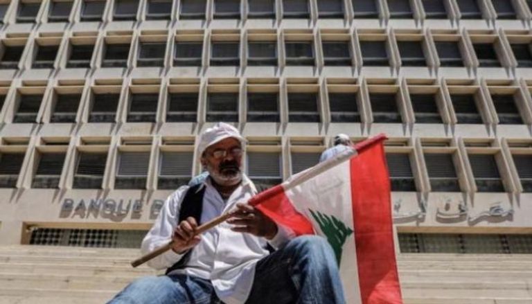 شخص يحمل علم لبنان أمام المصرف المركزي