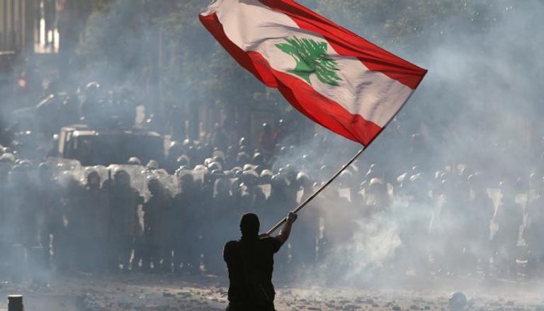 متظاهر يحمل علم لبنان في مواجهة قوات الأمن