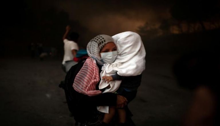 امرأة تحمل طفلها بعد حريق مخيم 