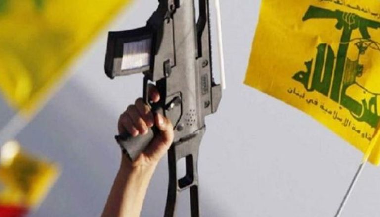 عنصر في حزب الله يرفع سلاحه وسط رايات المليشيا الموالية لإيران