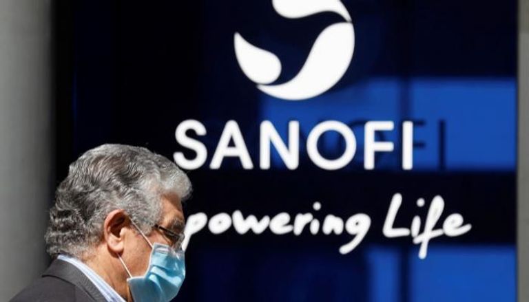 رجل يرتدي كمامة أمام شعار شركة "سانوفي"