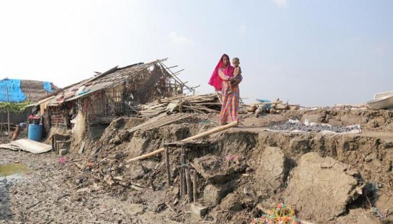 امرأة تحمل طفلا أمام منزل متضرر من الفيضانات في بنجلاديش