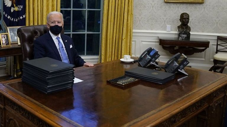 الرئيس الأمريكي جو بايده من خلف مكتبه - أرشيفية علبة أقلام أمام بايدن أثناء توقيعـه أوامر تنفيذية
