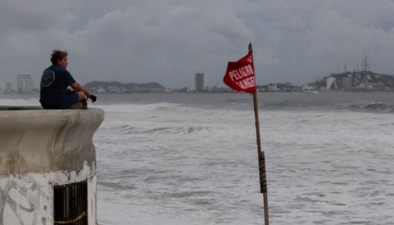 امرأة تراقب البحر بالقرب من علم تحذيري مع اقتراب عاصفة باميلا بالمكسيك
