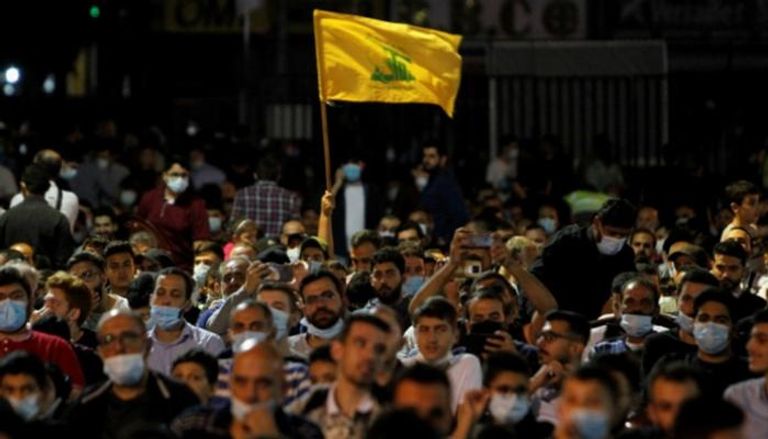 راية حزب الله يرفعها مشارك بأحد مؤتمرات المليشيات الموالية لإيران