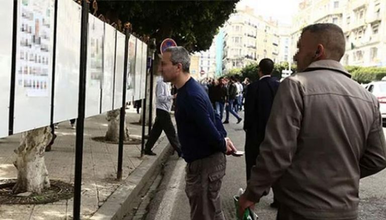 جزائريون أمام لافتات انتخابية لمرشحين خاصة بـ