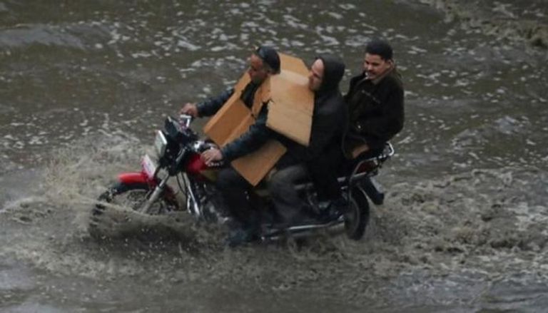 ثلاثة أشخاص يستقلون دراجة بخارية في شارع أغرقته مياه الأمطار (أرشيفية)