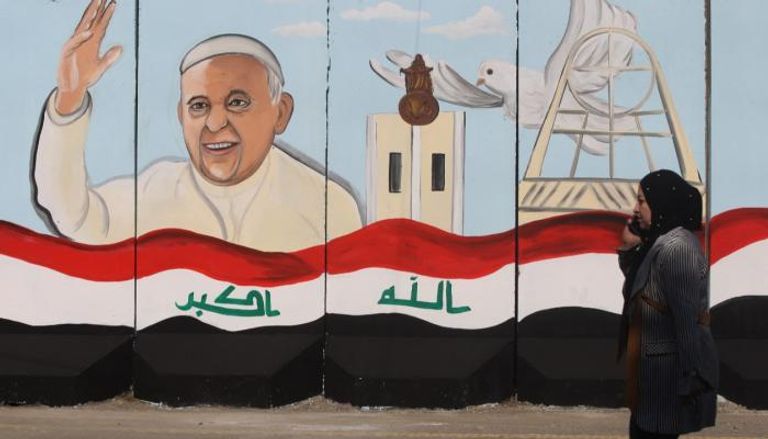 سيدة عراقية تسير أمام جدارية للبابا في بغداد 
