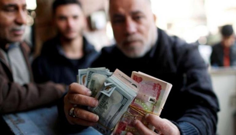 مواطن عراقي يمسك عملات ورقية من الدينار والدولار
