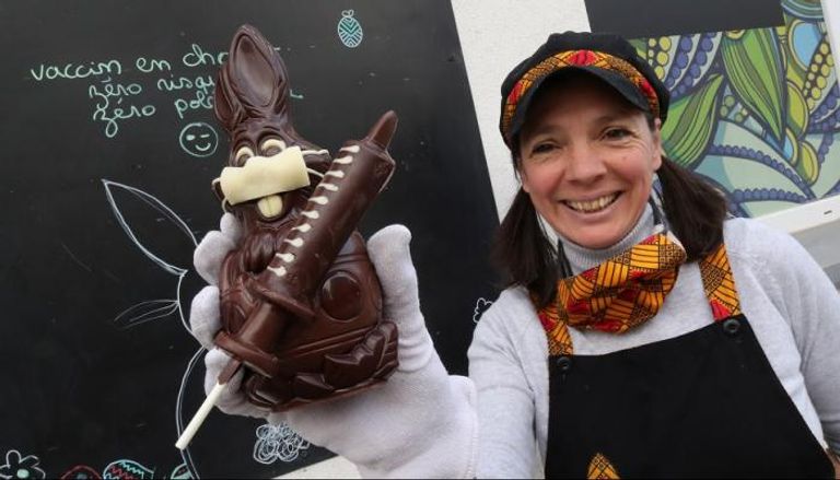 بلجيكية تحمل قالب شوكولاتة على هيئة أرنب يرتدي كمامة ويحمل حقنة