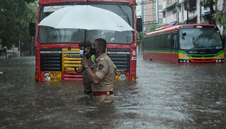 شرطي يساعد سائق نقل عام على عبور شارع غمرته المياه في مومباي