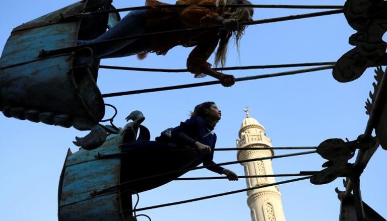 أطفال مصريون يلعبون بأحد الملاهي فيما تظهر في الخلفية مئذنة مسجد عمرو بن العاص في القاهرة