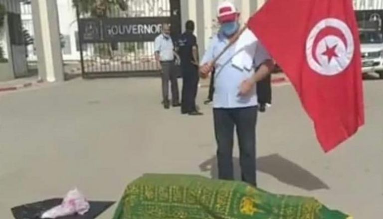 متظاهر تونسي يحمل علم بلاده أمام نعش احتجاجا على تردي الوضع الصحي