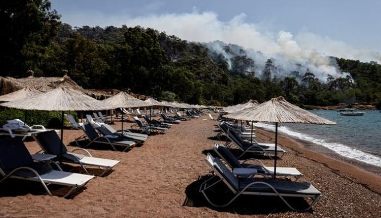 شاطئ فارغ في تركيا بينما يتصاعد دخان من غابة بسبب الحرائق