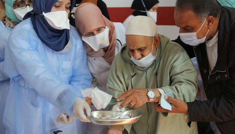 مسن مغربي يعقم يديه قبل تلقي جرعة من لقاح كورونا
