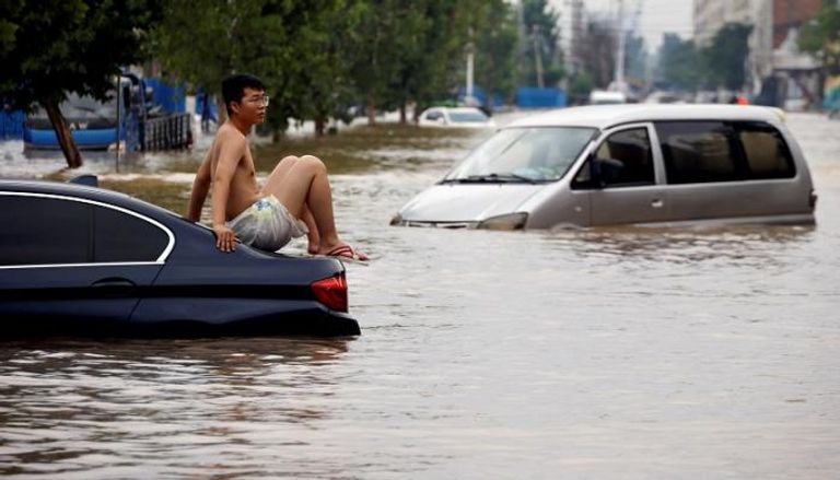 رجل يجلس على سيارة عالقة على طريق غمرته المياه