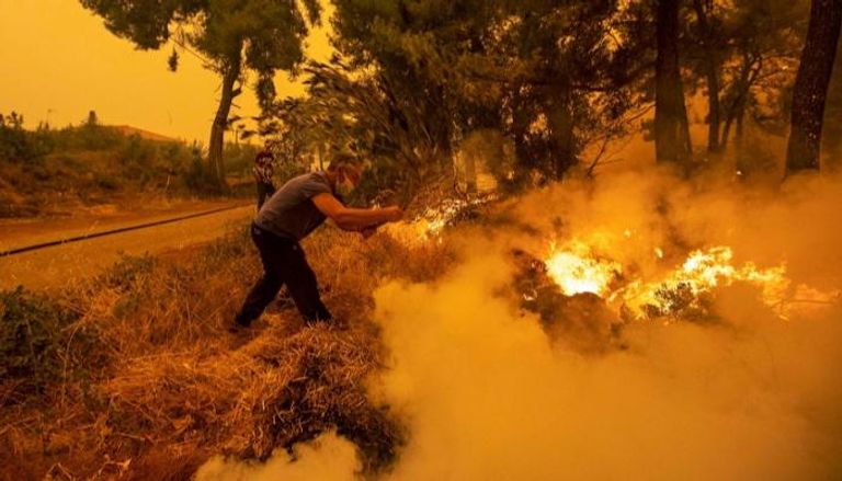رجل يحاول إخماد حريق في إحدى غابات اليونان