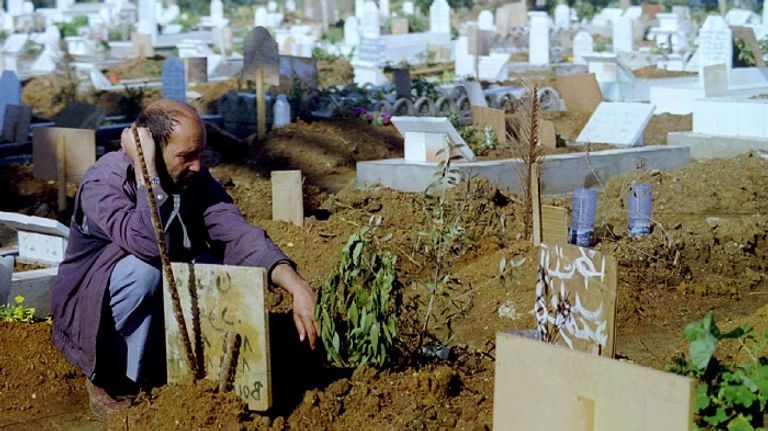 جزائري يجلس حزينا بجانب قبر عائلته التي قتلت جماعيا من الإرهابيين سنوات التسعينيات جزائرية تبكي.. ذبح الإرهابيون عائلتها بسنوات التسعينيات - أرشيفية