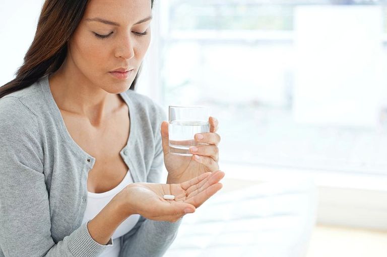 سيدة تمسك بعقار وكوب ماء قبل تناوله